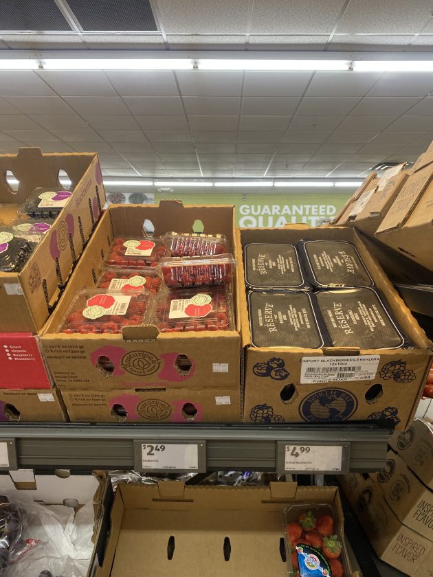 Display of fresh berries and packaged fruit in cardboard boxes.