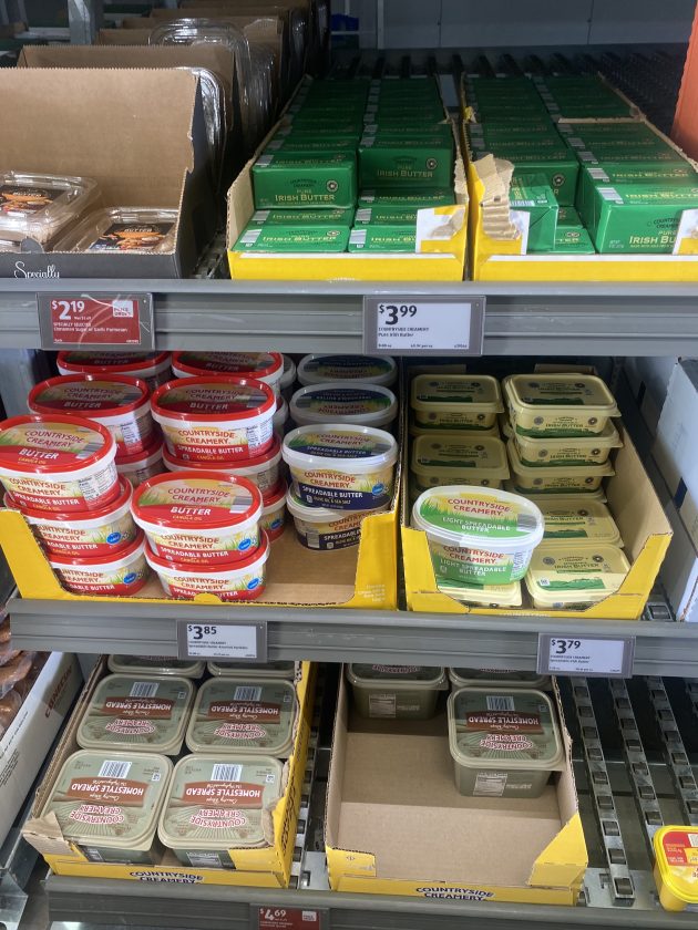 Refrigerated shelf stocked with Irish butter and Countryside Creamery spreadable butter tubs in different varieties with price tags visible.