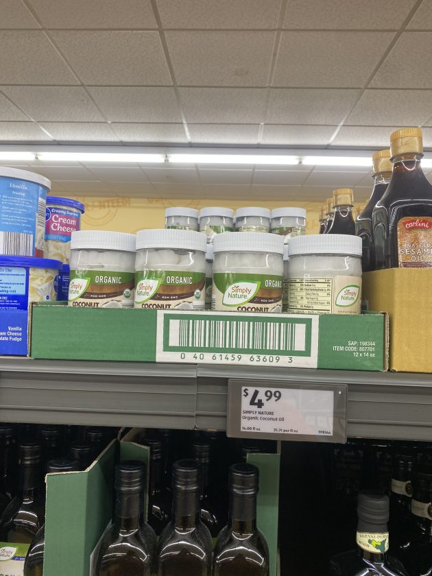 Shelf of jars labeled "Simply Nature Organic Coconut Oil" with a price tag reading "4.99" and a visible barcode on the display box.