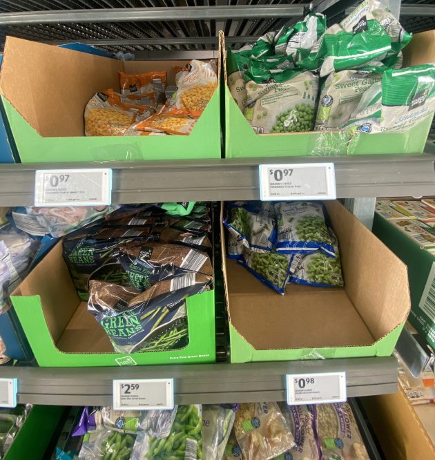 Freezer shelf with bags of frozen vegetables including peas and green beans in open boxes.