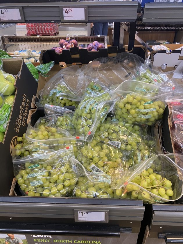 Open crate filled with bags of green grapes labeled "seedless grapes"