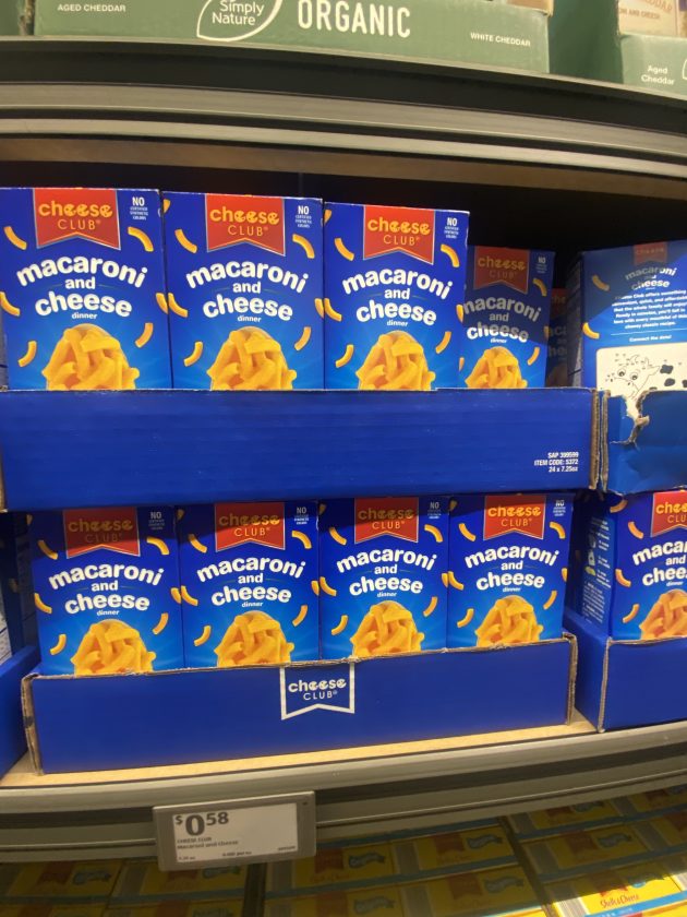Shelf stocked with blue boxes labeled "cheese club macaroni and cheese dinner" with a price tag. This quick meal is one of the best things to buy at Aldi.