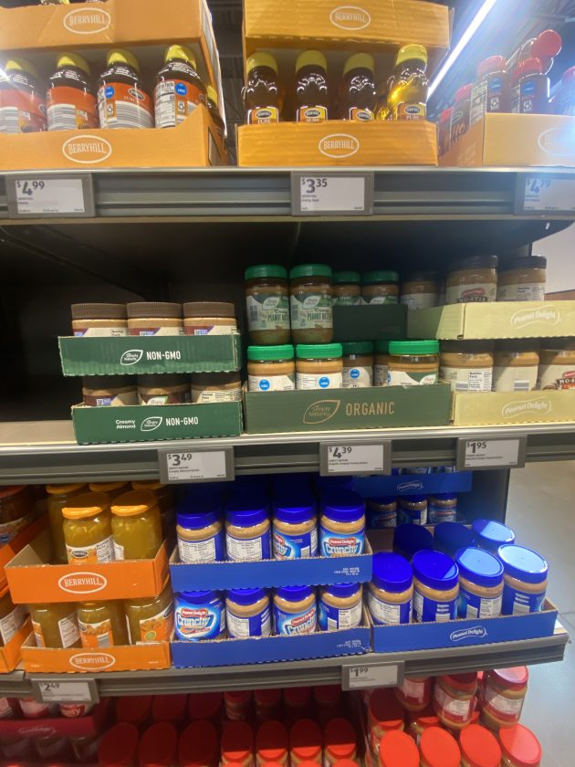 Shelves stocked with jars of peanut butter and spreads including organic and non GMO options with visible price tags like "3.49" and "4.39".