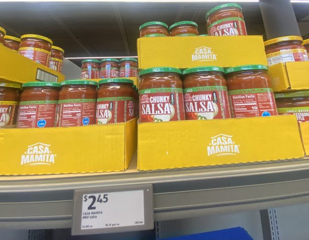 Jars of salsa labeled "Casa Mamita Chunky Salsa Mild" stacked in yellow boxes with a price tag of "2.45".