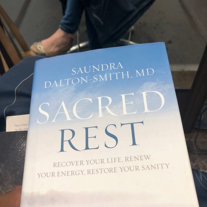 Book cover for "Sacred Rest. Recover Your Life, Renew Your Energy, Restore Your Sanity" by Saundra Dalton-Smith displayed on a person's lap.