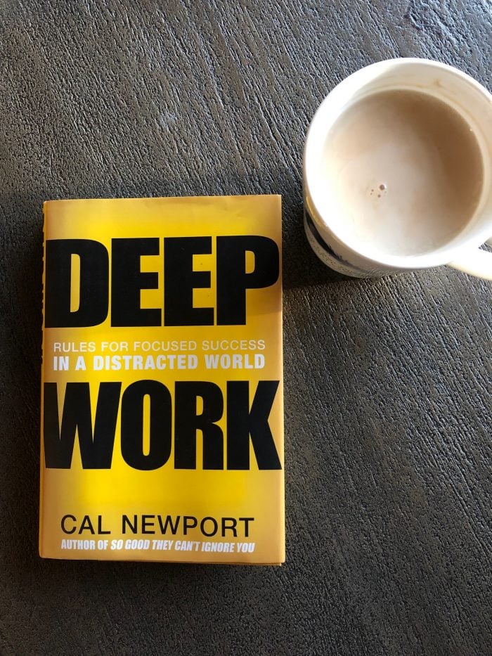 Copy of "Deep Work. Rules for Focused Success in a Distracted World" by Cal Newport beside a mug of coffee on a dark tabletop. Frequently recommended among the top non-fiction books on productivity and focus.