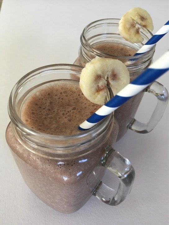 Two mason jars filled with creamy banana shakes and topped with banana slices on the rim.