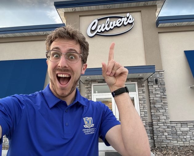 Zachary smiling outside a Culver's restaurant points up at the restaurant sign while taking a selfie. T