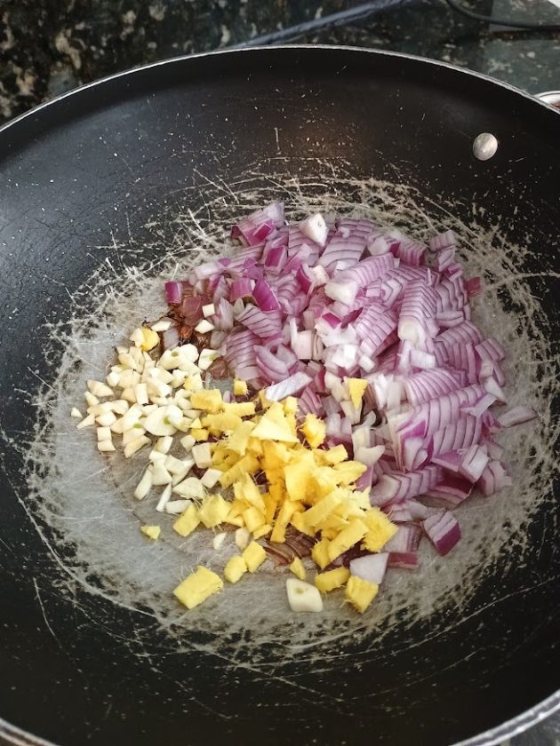 Chopped red onions, garlic, and ginger placed in a pan ready to be sautéed.