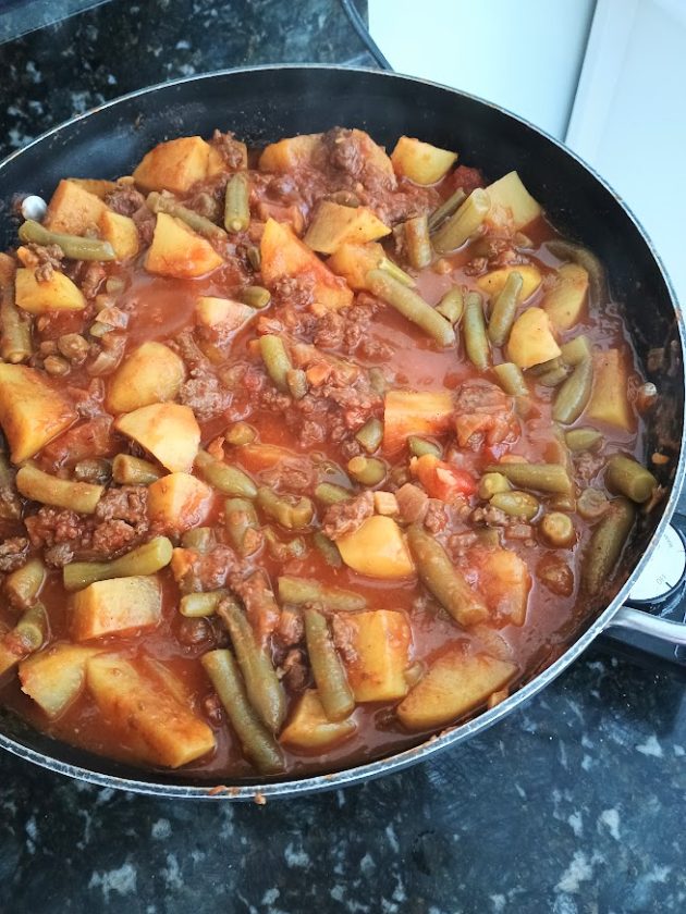 Finished kima curry with potatoes and green beans simmering in a thick red gravy in a large pan.