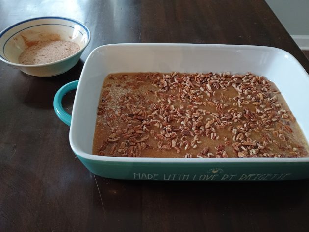 Baking dish filled with melted butter and brown sugar mixture topped with pecans.
