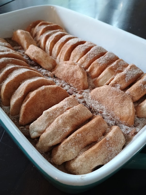 Unbaked biscuit dough pieces arranged upright in a baking dish and coated in cinnamon sugar, showing the preparation step.