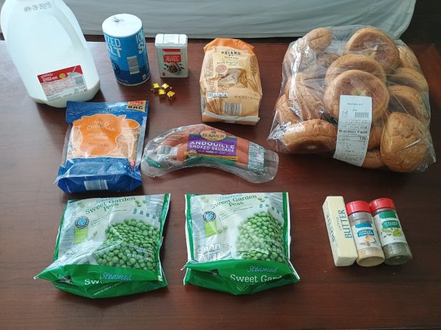 Ingredients laid out on a table including milk, shredded cheese, kielbasa sausage, pasta, peas, butter, and seasonings for making a kielbasa pasta skillet.