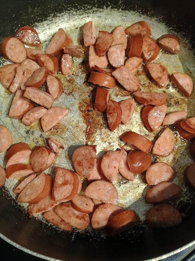 Sliced kielbasa sausage browning in a pan with butter, showing the first step of cooking a kielbasa skillet recipe.