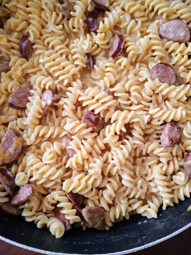 Tight view of creamy rotini pasta and sliced kielbasa pieces in a skillet, emphasizing the rich sauce and browned sausage in this kielbasa skillet.