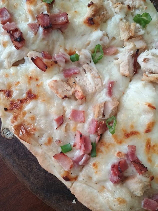 Close up of chicken alfredo pizza with melted cheese, browned spots, chunks of chicken, bacon bits, and green onions.