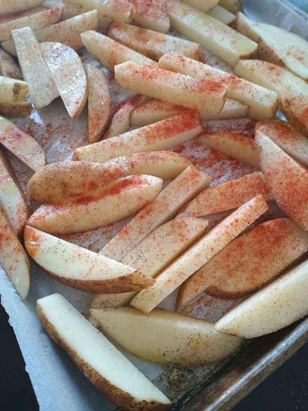Raw potato wedges spread on a baking tray, coated with seasoning before roasting.