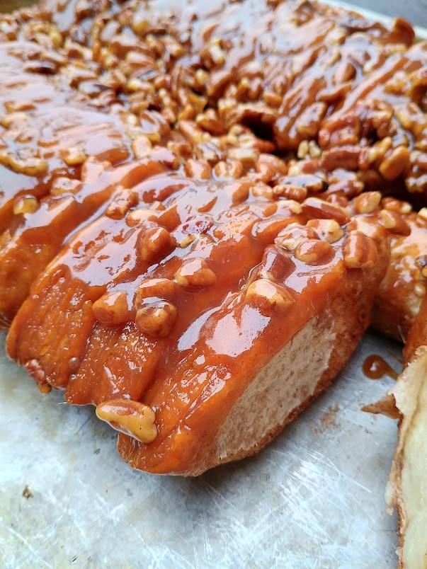 Close up of baked monkey bread pieces coated in thick caramel sauce and chopped pecans, showing the sticky texture and pull apart layers of this easy monkey bread recipe.