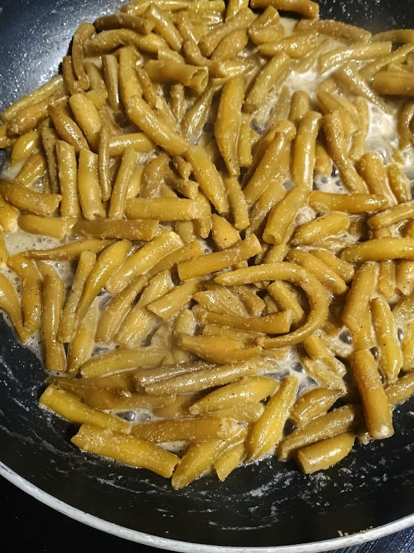 Cooked green beans simmering in a skillet with butter sauce.