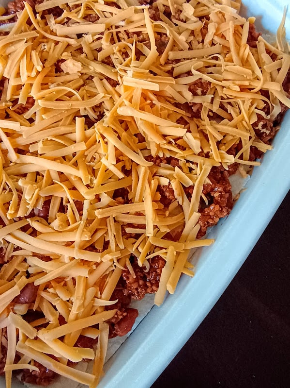 Unbaked taco pie layered in a casserole dish and covered with shredded cheddar cheese.