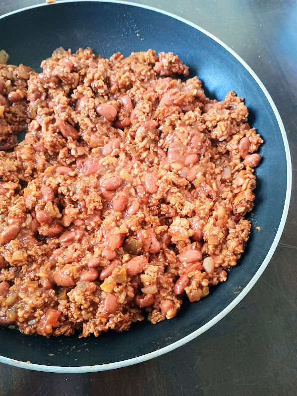 Skillet filled with seasoned ground meat, beans, onions, and tomatoes cooking for Mexican lasagna.