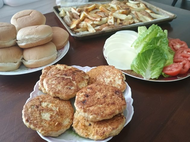Chicken patties plated with burger buns, cheese, lettuce, tomato, and a tray of fries in the background.