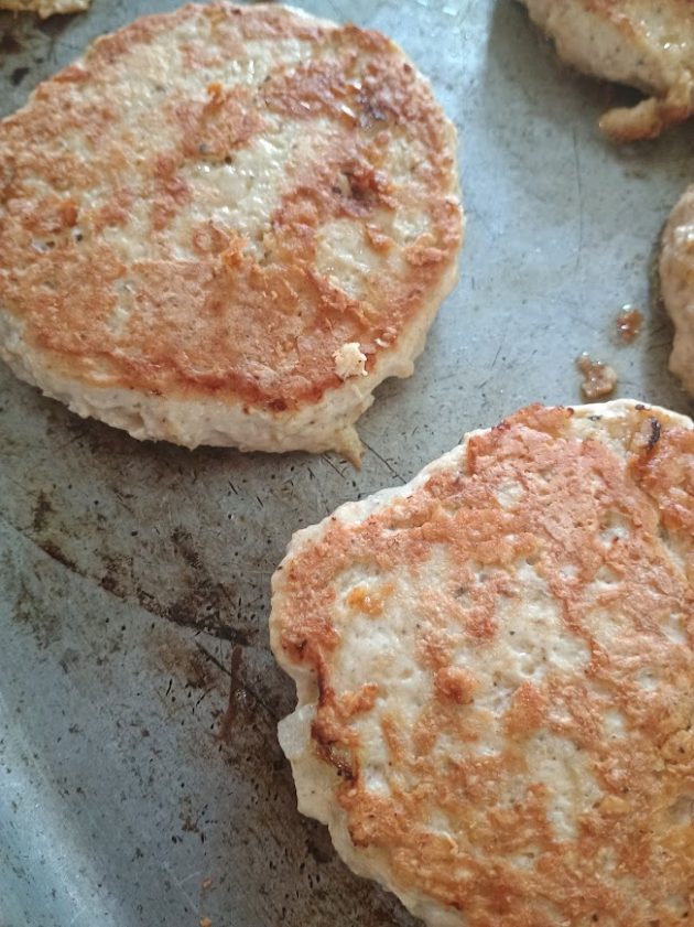 Two chicken patties cooking on a metal baking sheet.