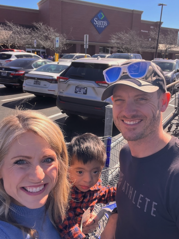 Smiling family selfie with Crystal Paine in a Sam’s Club parking lot with the store sign visible behind them and cars parked in rows.