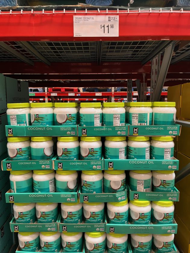 Stacked jars labeled "COCONUT OIL" with a price sign above reading "$11.98" in a warehouse style shelf display.