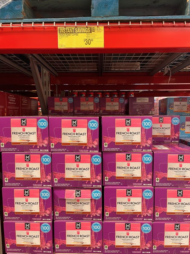 Display of purple boxes labeled "FRENCH ROAST single serve cups" with a yellow sign above reading "INSTANT SAVINGS $30.98.