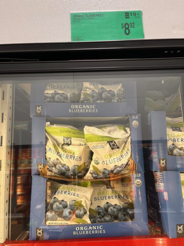 Freezer display of bags labeled "ORGANIC BLUEBERRIES" with a green price sign above reading "$8.92" and boxes marked "3 LB."