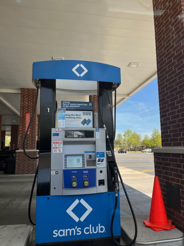 Gas pump with "sam’s club" branding under a covered station with a red cone nearby and payment screen visible.