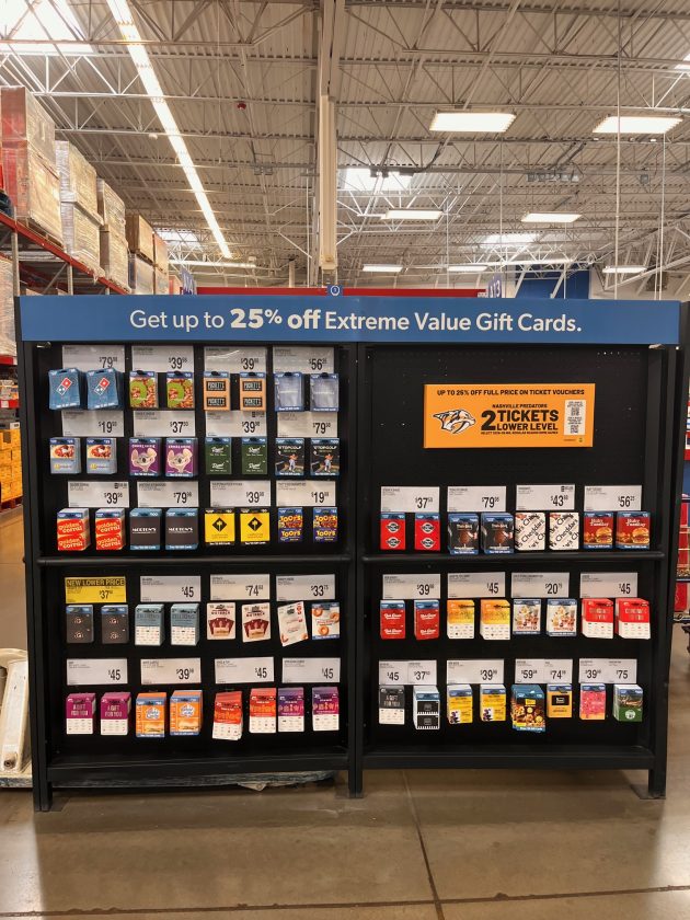 Wide display of gift cards with a sign reading "Get up to 25% off Extreme Value Gift Cards" and multiple brand options arranged in rows.