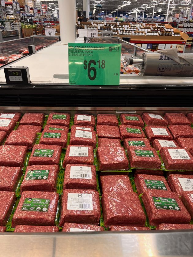 Refrigerated meat case filled with packages labeled "ORGANIC GROUND BEEF" with a green sign reading "$6.18 per lb" displayed above.