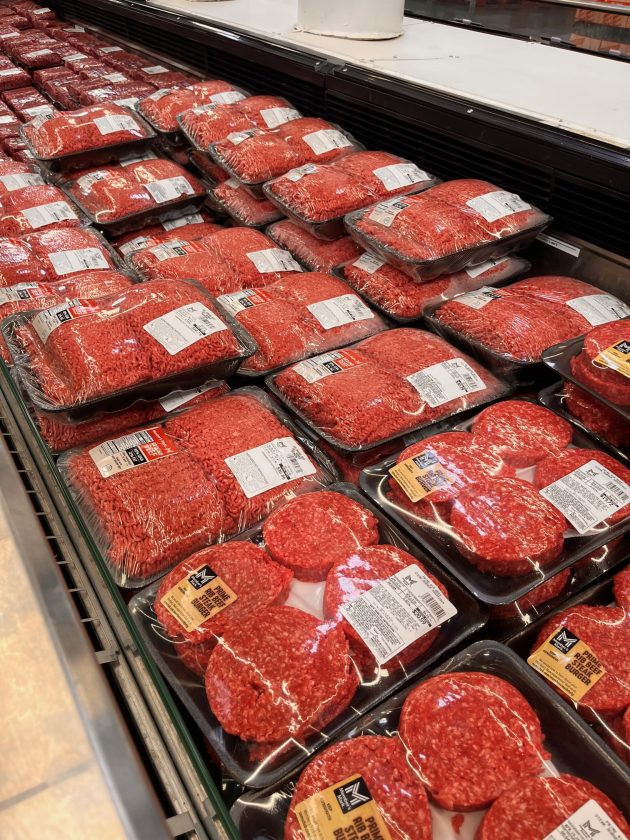 Meat case filled with trays of ground beef and burger patties wrapped in plastic and arranged in rows inside a refrigerated display.