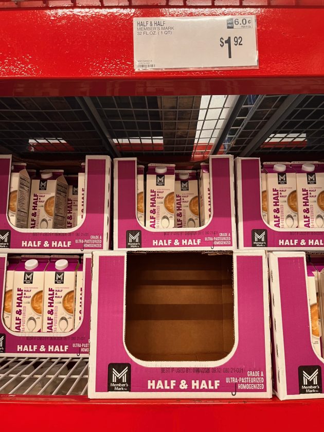 Large shelf display of pink cartons labeled "HALF & HALF" with a price sign reading "$1.92" and one empty slot in the center of the case.