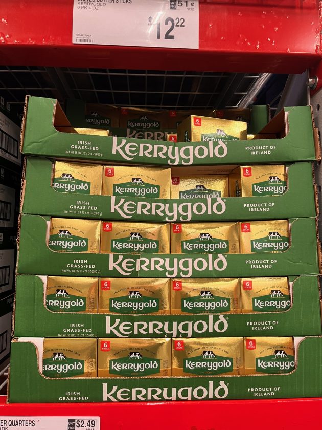 Stacked boxes of Kerrygold butter labeled "IRISH GRASS-FED" and "PRODUCT OF IRELAND" with a price sign above reading "$12.22.