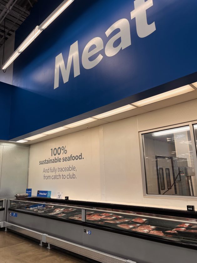 Blue wall sign reading "Meat" above a refrigerated meat section with text on the wall that says "100% sustainable seafood. And fully traceable, from catch to club."