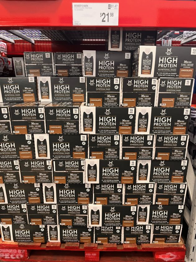 Large pallet display of boxes labeled "HIGH PROTEIN nutritional shake chocolate 30g protein 15 pack" stacked in rows.