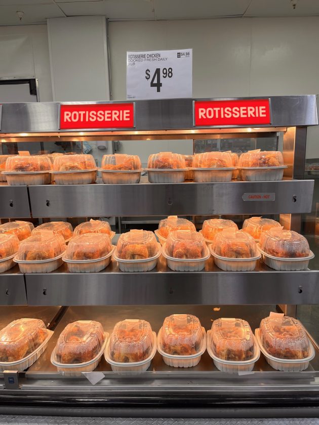 Heated display case filled with packaged rotisserie chickens under red signs reading "ROTISSERIE" and a price sign above that reads "$4.98."
