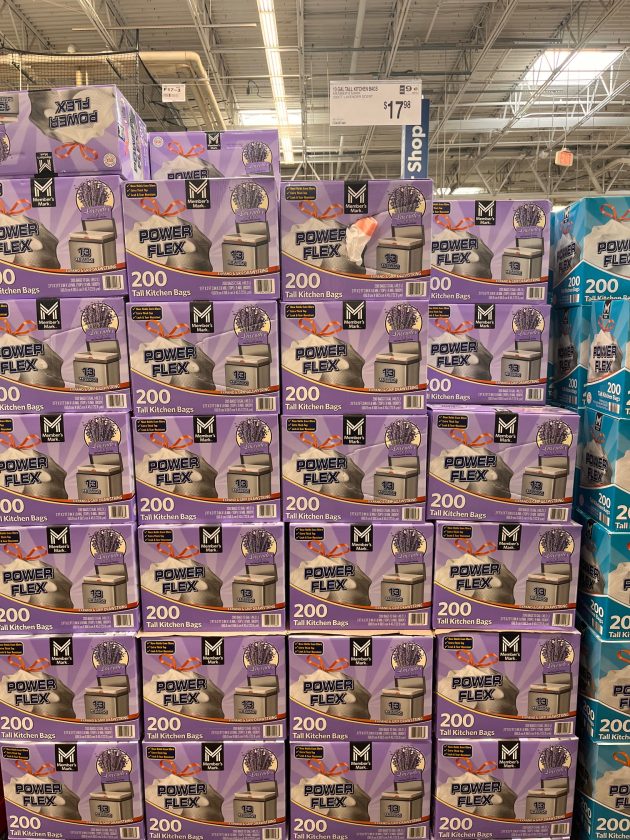 Pallet stacked display of purple boxes labeled "POWER FLEX 200 Tall Kitchen Bags" with price signage hanging above.