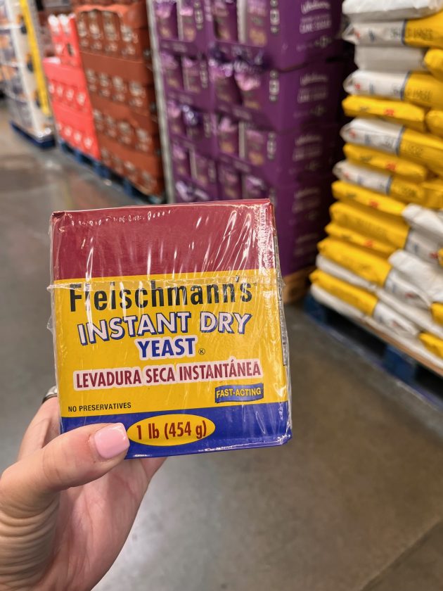 Hand holding a package labeled "Fleischmann’s INSTANT DRY YEAST" with text "LEVADURA SECA INSTANTÁNEA FAST-ACTING 1 lb 454 g" visible on the front.