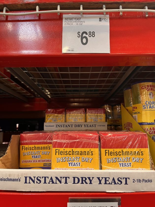 Shelf stocked with boxes labeled "Fleischmann’s INSTANT DRY YEAST" with a price sign above reading "$6.88" and text "2-1 lb packs."