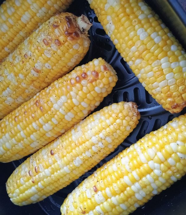 Several ears of corn on the cob cooking in an air fryer basket.