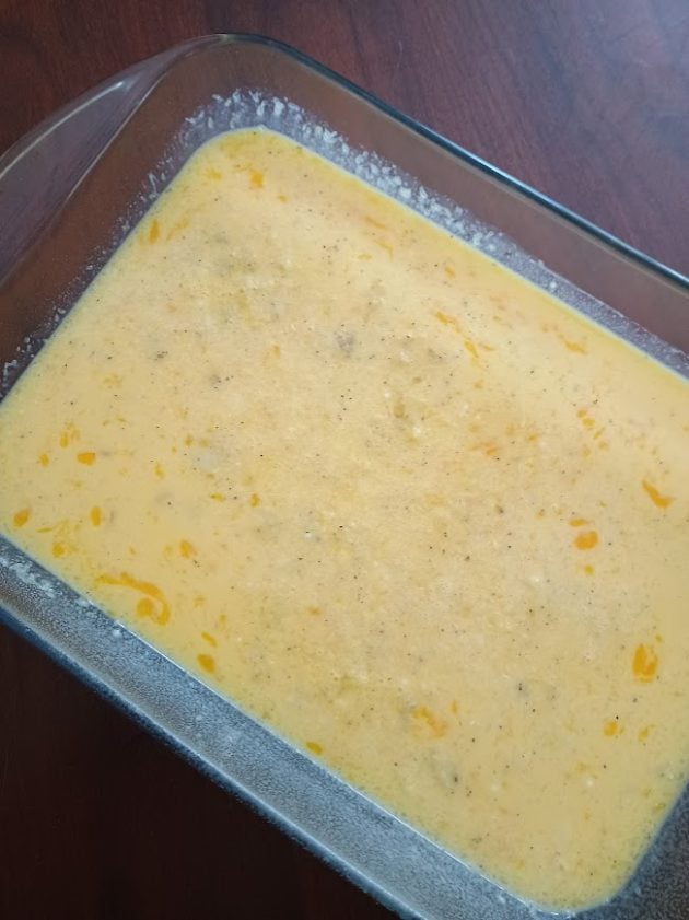Unbaked scrambled egg mixture seasoned and poured into a glass baking dish before cooking.