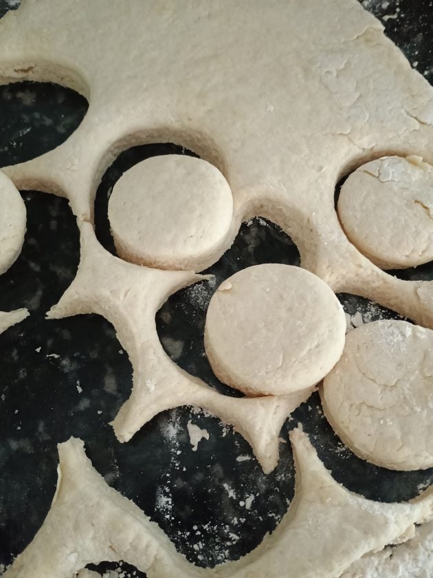 Rolled biscuit dough cut into circles on a floured surface before baking.