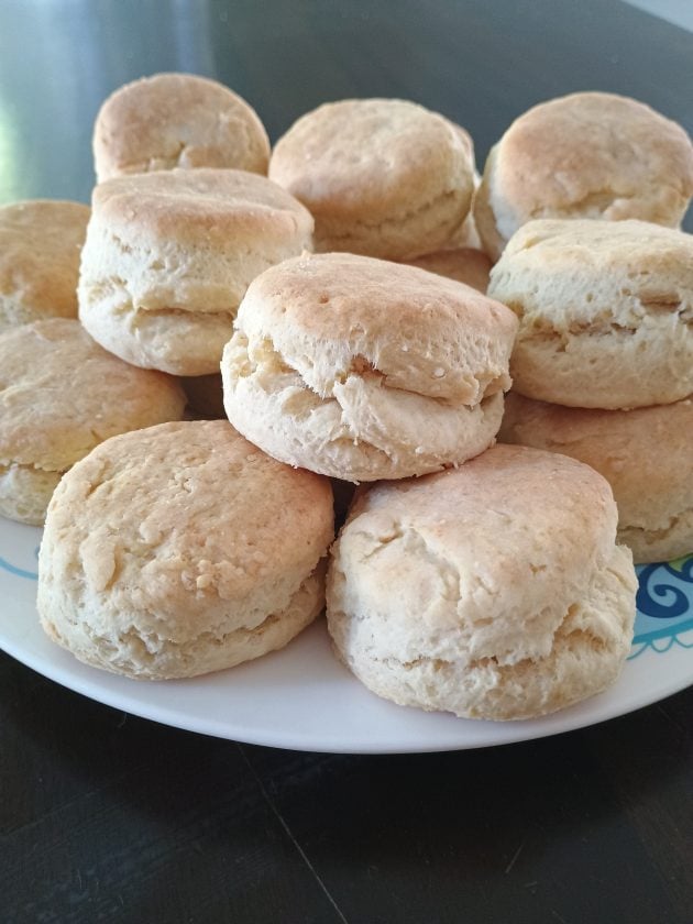 Freshly baked homemade biscuits piled on a white plate with golden tops.