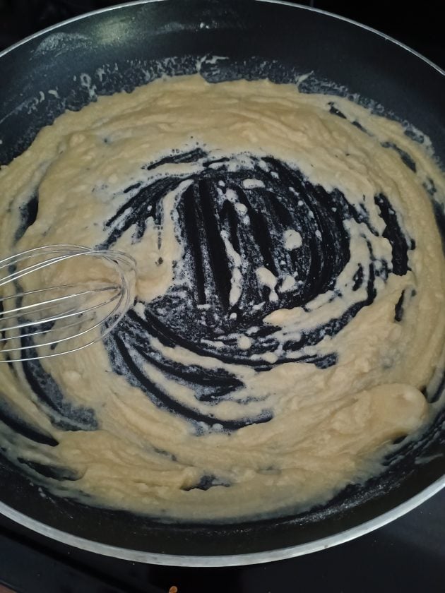 Thick biscuit gravy mixture being whisked in a skillet as it cooks down on the stovetop.