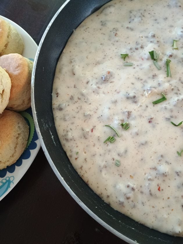 Close up of creamy sausage gravy in a black skillet with bits of sausage.