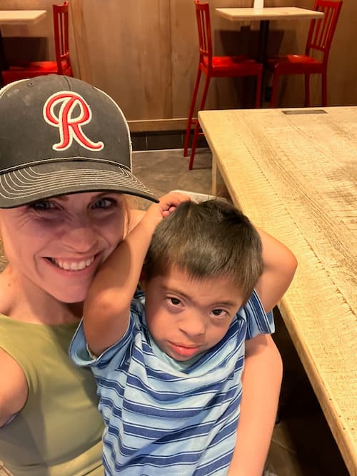 Smiling adult and child sit together at a restaurant table while taking a selfie.